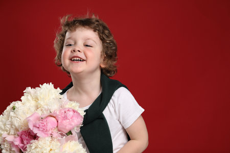 Cute little boy with bouquet of beautiful peonies on red background. Space for textの写真素材