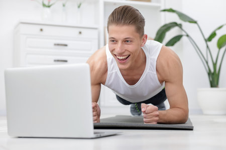 Man doing plank exercise during online class with coach at home. Sport and healthy lifestyleの写真素材