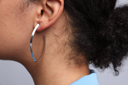 Young woman wearing elegant silver earring on light gray background, closeup