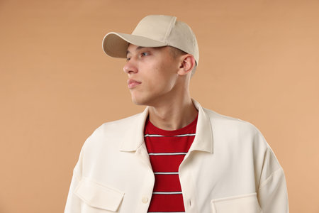 Young man in stylish baseball hat on beige background