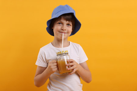 Cute little boy in panama hat drinking juice on orange background. Refreshing drinkの写真素材