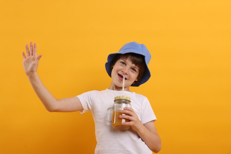 Happy little boy in panama hat with mason jar of juice on orange background. Refreshing drinkの写真素材