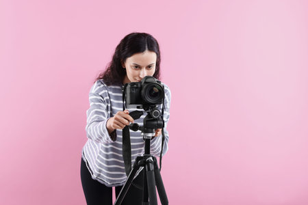 Woman with professional video camera on pink background, space for text