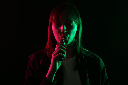 Woman using electronic smoking device in neon lights on black background