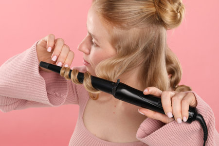 Woman curling her hair on pink backgroundの写真素材