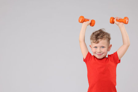 Little boy exercising with dumbbells on gray background, space for textの写真素材