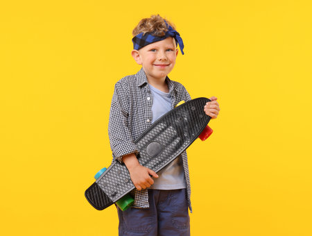 Little boy with penny board on yellow backgroundの写真素材