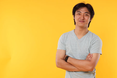 Portrait of handsome Asian man with crossed arms on yellow background. Space for textの写真素材