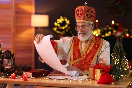Saint Nicholas with gift list at desk in room decorated for Christmasの写真素材