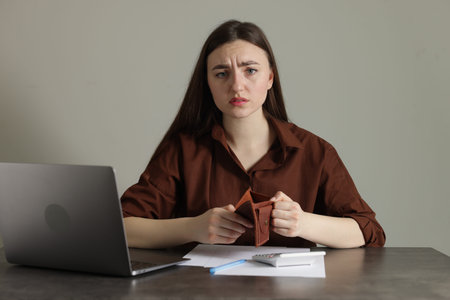 Upset woman with empty wallet at grey table. Financial problems