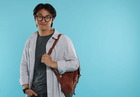 Handsome Asian man in glasses with backpack on light blue background. Space for textの写真素材