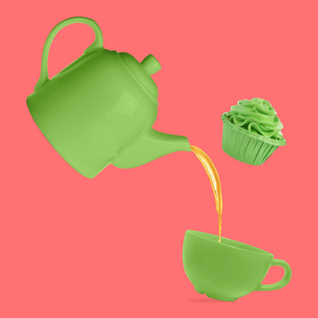 Pouring tea from green teapot into cup and cupcake against coral color backgroundの写真素材