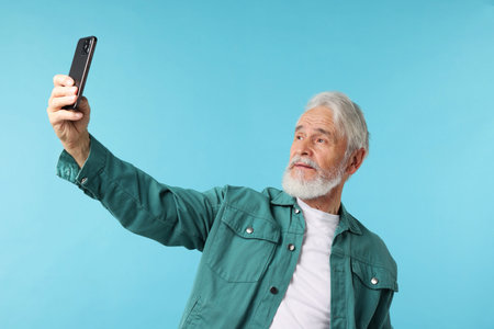 Elderly man taking selfie on light blue background