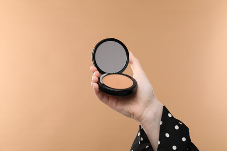 Woman holding open face powder with mirror on beige background, closeupの写真素材