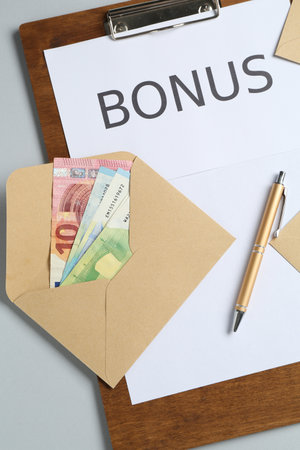 Clipboard with word Bonus and envelope with money on light grey background, flat layの写真素材