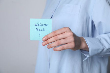 Woman holding paper note with words Welcome Back on grey background, closeupの写真素材