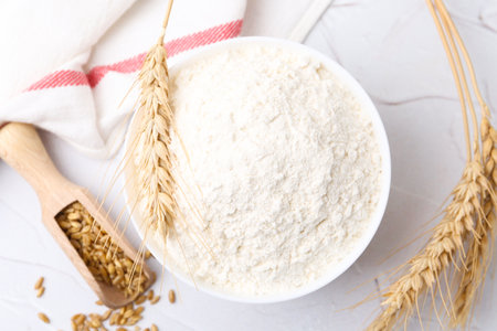 Wheat flour in bowl, grains and spikes on white table, flat layの写真素材