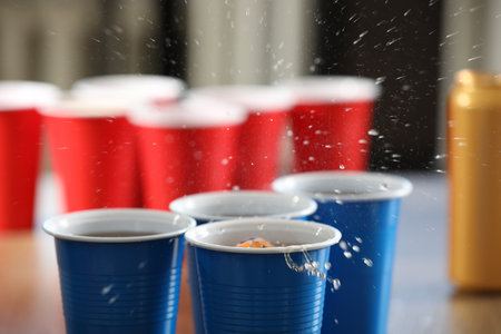Beer pong game. Plastic cups with drinks and ball on table, closeupの写真素材