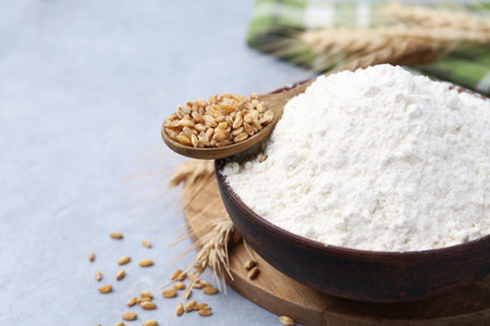 Wheat flour in bowl, grains and spikes on grey table, closeup. Space for textの写真素材