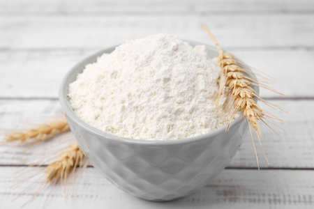 Wheat flour in bowl and spikes on light wooden table, closeupの写真素材