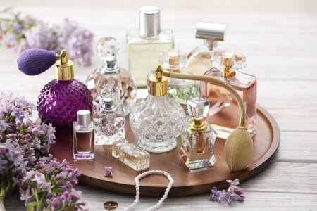 Bottles of perfumes, accessories and lilac flowers on white wooden table