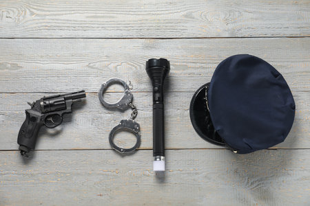 Police cap, flashlight, handcuffs and gun on grey wooden table, flat layの写真素材