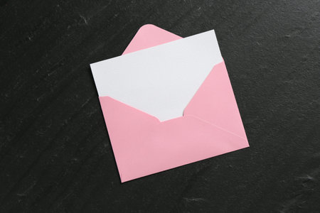 Blank invitation card and envelope on black table, top view. Space for design