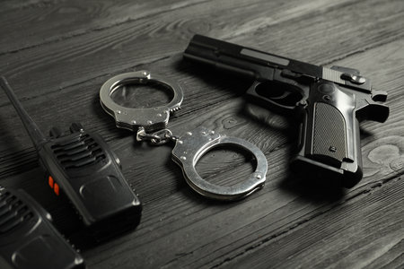 Gun, handcuffs and walkie talkies on black wooden table, closeup. Police equipmentの写真素材