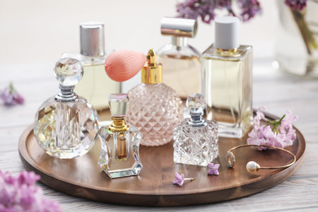 Bottles of perfumes and lilac flowers on white wooden table, closeup