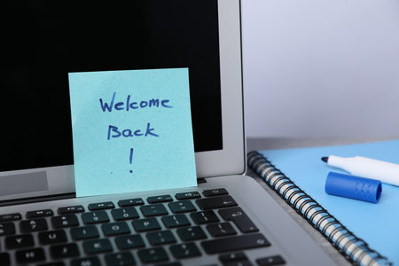 Sticky note with phrase Welcome Back, laptop, marker and notebook on table, closeupの写真素材