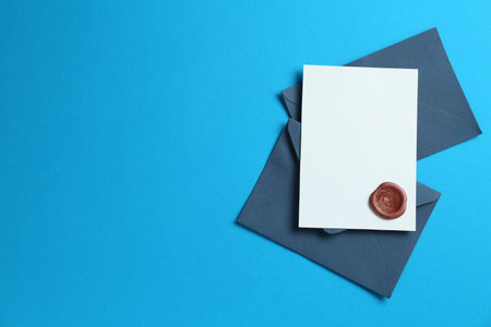 Blank invitation card with wax seal and envelopes on light blue background, flat lay. Space for designの写真素材