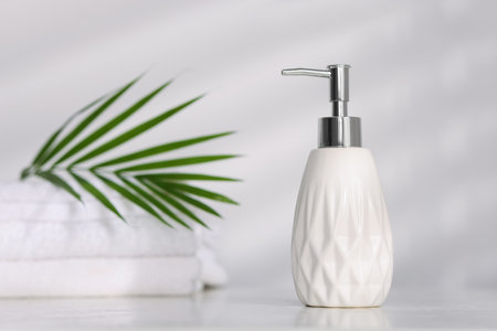 Liquid soap in bottle, towels and palm leaf on white table indoorsの写真素材