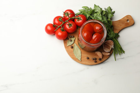 Tasty pickled tomatoes in jar and ingredients on white marble table, flat lay. Space for textの写真素材