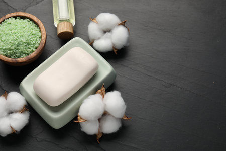 Soap bar, cosmetic products and cotton flowers on black table, flat lay. Space for textの写真素材