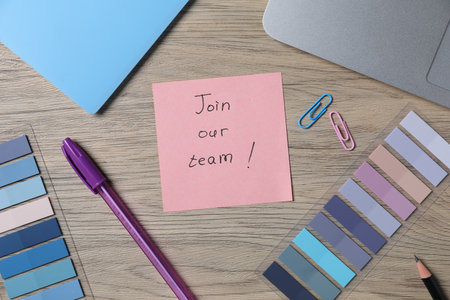Paper note with phrase Join Our Team, laptop and stationery on wooden table, flat layの写真素材