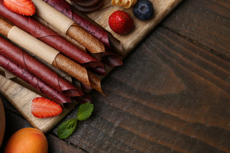 Tasty candied leather rolls, fruits and berries on wooden table, flat lay. Space for textの写真素材