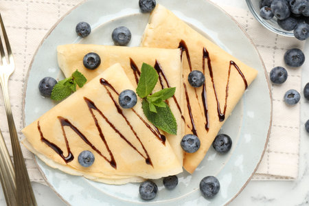 Tasty crepes with blueberries, chocolate sauce and mint served on table, flat layの写真素材