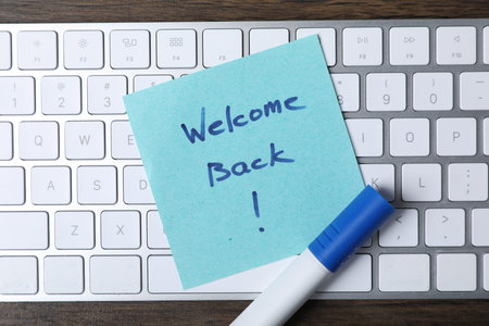 Paper note with phrase Welcome Back, marker and keyboard on table, top viewの写真素材