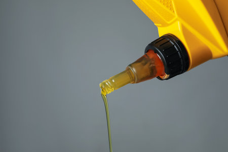 Pouring motor oil from yellow canister on grey background, closeup. Space for textの写真素材