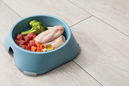 Feeding bowl with natural raw products for pet on white wooden floor, closeup. Space for textの写真素材