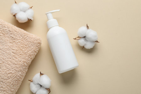 Bottle of liquid soap, cotton flowers and towel on beige background, flat lay. Space for textの写真素材