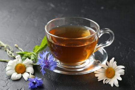 Aromatic herbal tea in glass cup, different flowers and mint on black table, closeupの写真素材