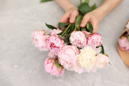 Florist making beautiful bouquet of peonies at gray marble table, closeupの写真素材
