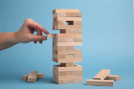 Lviv, Ukraine - December 04, 2023: Woman playing Jenga on light blue background, closeupの写真素材
