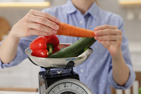 Woman weighing vegetables on kitchen scale indoors, closeupの写真素材