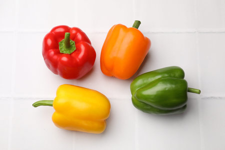 Fresh colorful bell peppers on white tiled table, flat lay