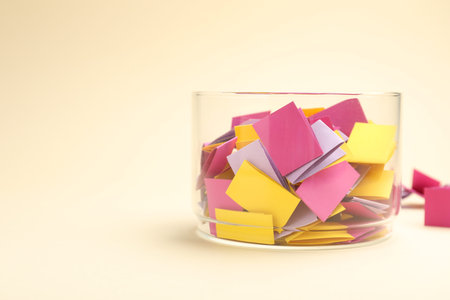 Jar with colorful pieces of paper on beige background, closeup. Space for text