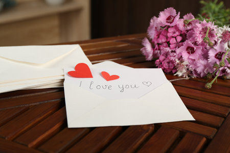 Card with phrase I Love You, letters, red hearts and flowers on wooden table indoors, closeupの写真素材