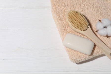 Soap bar, cotton flower, brush and towel on white wooden table, top view. Space for textの写真素材