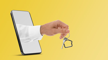 Real estate services online. Man's hand with key sticking out from smartphone on yellow background. Banner design with space for textの写真素材